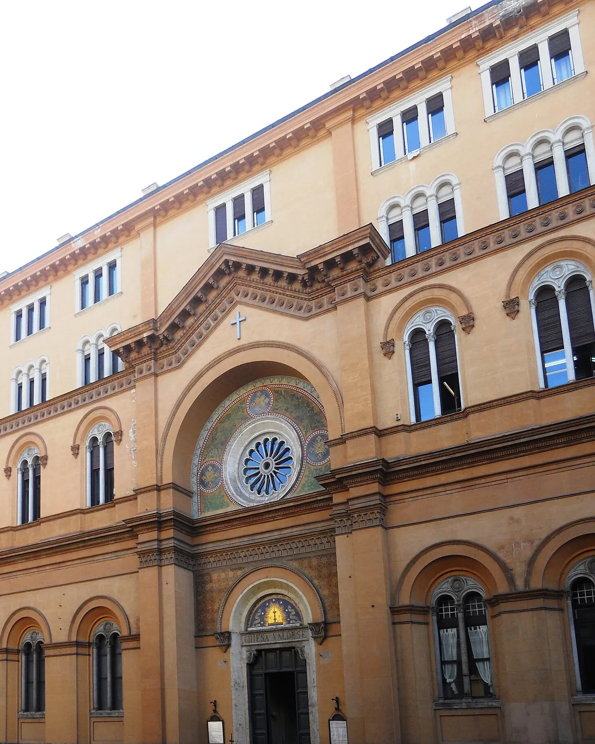 Průčelí valdenského kostela na Via Quattro Novembre v Římě: kruhové okno v mozaikovém oblouku nad vchodem s nápisem Chiesa Valdese, zasazené do okrového průčelí paláce.